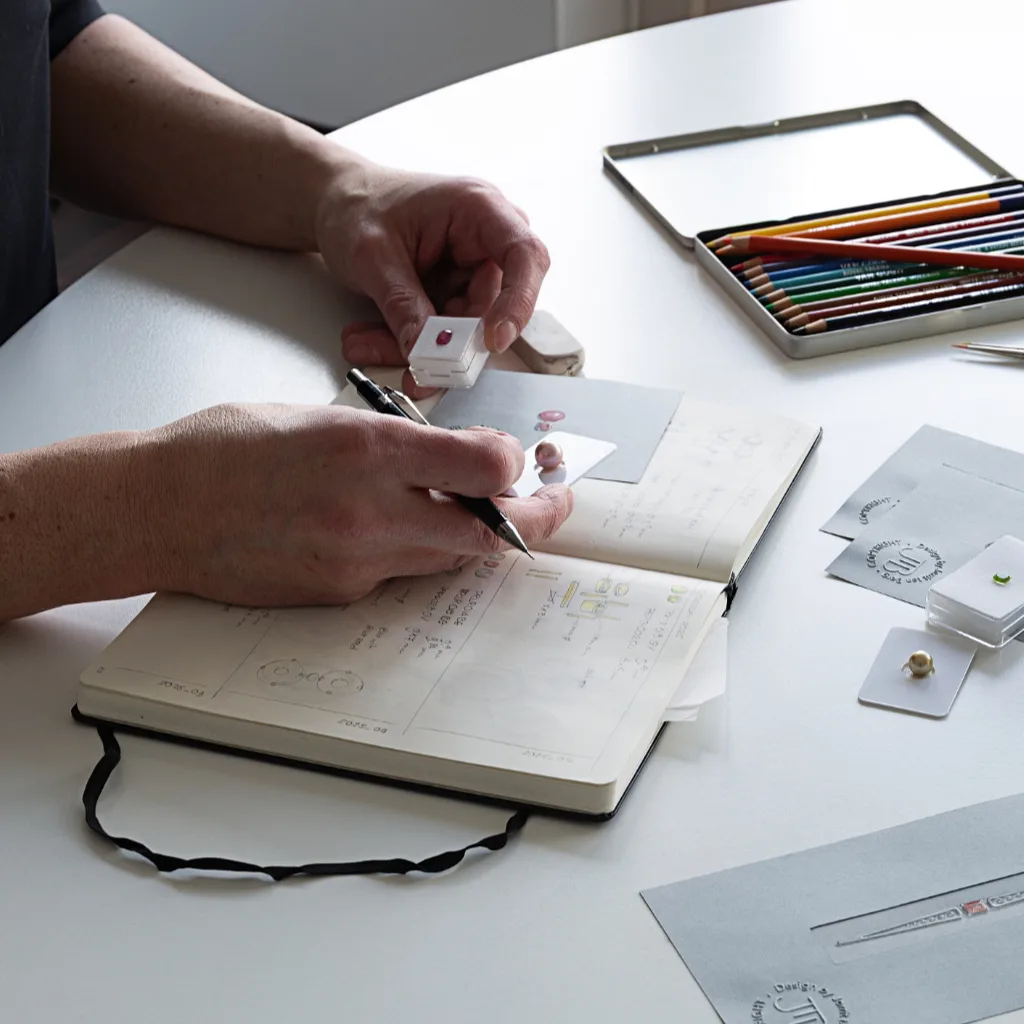 Ontwerper aan tafel met meerder juwelen ontwerpen en een selectie van bijpassende edelstenen