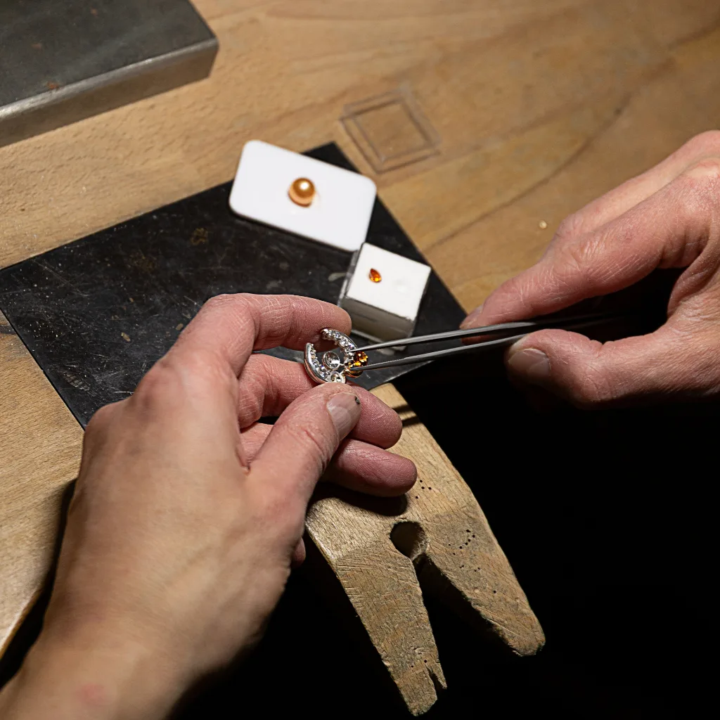 Hand van de maker past een edelsteen in een broche