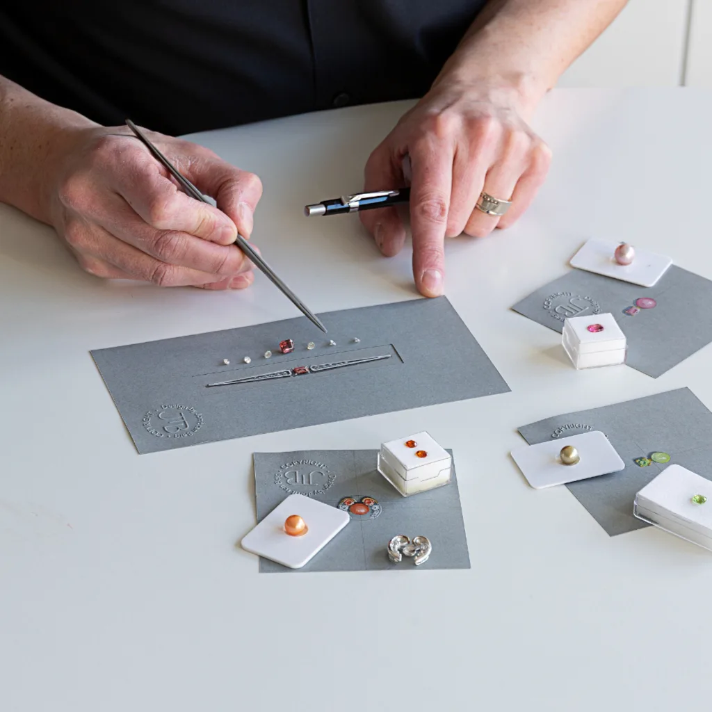 Ontwerper met op tafel voor zich juwelen ontwerpen en bijpassende stenen